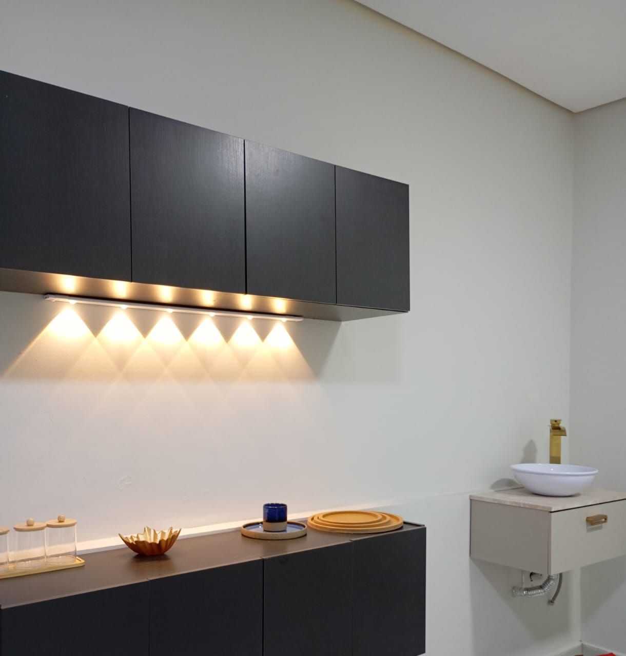 Sala de atendimento com armários pretos, iluminação quente em LED e cuba com torneira dourada