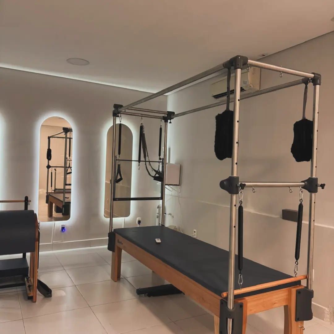 Cadillac de Pilates em primeiro plano, com espelhos em arco iluminados ao fundo